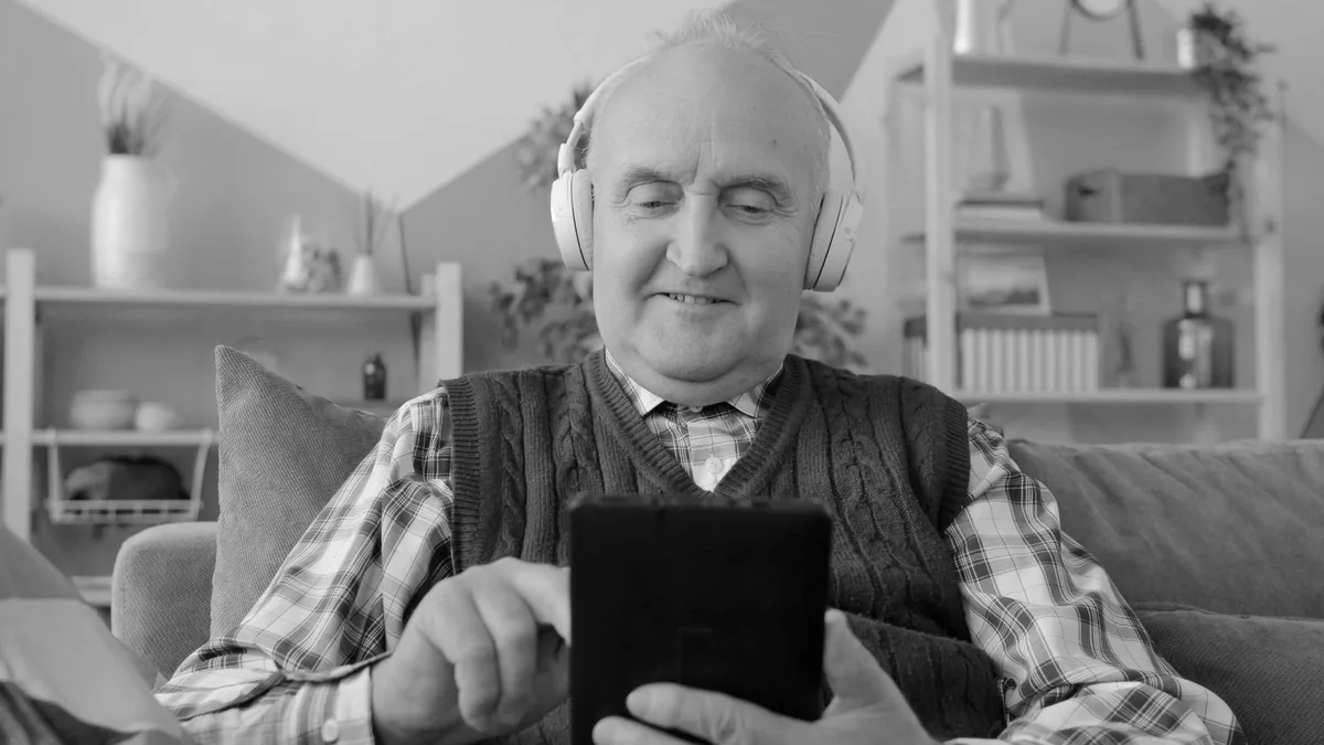 Older man at home wearing headphones and smiling at his phone